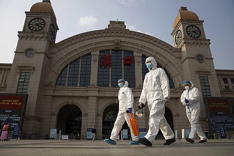 Workers in protective overalls walk past the Hankou railway station on the eve of its resuming outbound traffic in Wuhan in central China's Hubei province. (Photo | AP)