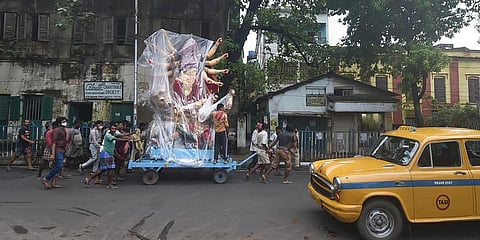 Devotees carry an idol of Durga shielded in a plastic cover to protect from rain on a city street to install at a community puja pandal for worship ahead of Durga Puja, Kolkata, Tuesday (Photo | PTI)