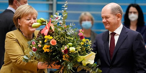 German Chancellor Angela Merkel (L) receives a bouquet from Vice Chancellor and Finance Minister Olaf Scholz (R) prior to the cabinet meeting at the chancellery in Berlin. (Photo | AP)
