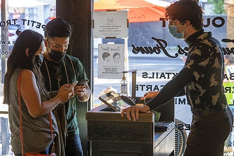 Restaurant host Joey Tyler, right, verifies arriving patrons' Digital COVID-19 Vaccine Records at French restaurant Petit Trois. (Photo | AP)