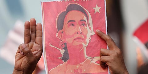 Myanmar nationals living in Thailand hold pictures of Aung San Suu Kyi gesture with a three-fingers salute, a symbol of resistance infront of Myanmar embassy in Bangkok. (File Photo | AP)