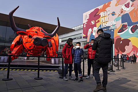 A man and a child put on their face mask to help curb the spread of the coronavirus after taken a souvenir photo near a Year of the Ox statue on display. (Photo | AP)