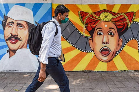 A man wearing a face mask as a precaution against Covid-19 walks past a mural at Lalbaug in Mumbai. (File Photo | PTI)