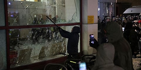 A protester smashes a window with a stick outside Bridewell Police Station, in Bristol, England. (Photo | AP)