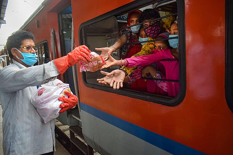 A railway staff member distributes food packets among migrants sitting in Shramik Special train to reach their native places during ongoing COVID-19 lockdown at Prayagraj Railway Station Sunday May 31