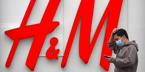 A man uses his smartphone as he walks past an H&M clothing store at a shopping mall in Beijing, Friday, March 26, 2021. (Photo | AP)