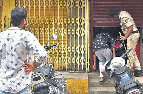 A policeman forces a shop to shut down on SP Road in Bengaluru on Thursday