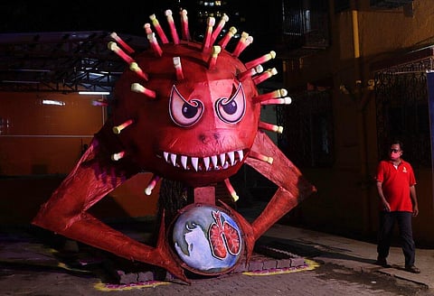 A man wearing a mask walks past an effigy of Coronavirus. (Photo | AP)