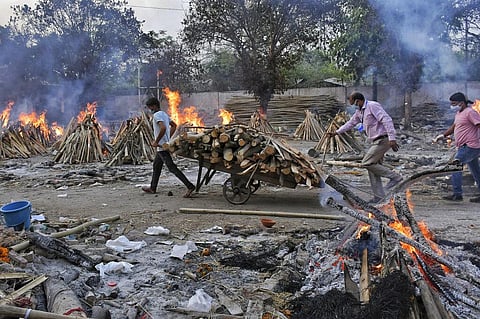 A worker carries wood on a hand cart as multiple funeral pyres of COVID-19 victims burn at a crematorium on the outskirts of New Delhi. (Photo | AP)