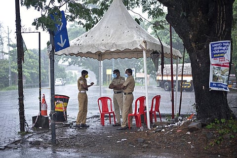 Policemen enforcing a lockdown to curb the spread of coronavirus stand beneath a rain shelter  (Photo | AP)