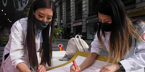 Dr. Michelle Lee (L) a radiology resident, and Ida Chen (R) a physician assistant student, prepare posters they carry at rallies protesting anti-Asian hate in New York's Chinatown. (Photo | AP)