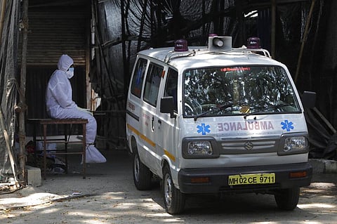 A health worker in personal protective equipment sits beside an ambulance as he takes a break outside a field hospital in Mumbai. (Photo | AP)