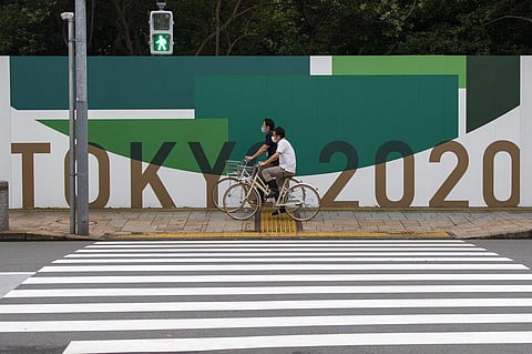 Men wearing face masks ride bicycles along the wall installed to close off a park being prepared for the Olympics and Paralympics Games in Tokyo on Thursday, July 1, 2021. (Photo | AP)