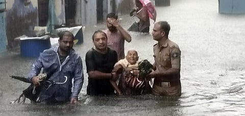 Locals help an elderly woman move through a waterlogged street as heavy rain disrupts normal life, in Rajkot. (Photo| ANI)