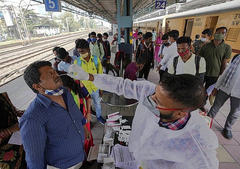 A health worker collects a swab sample from a traveler at a train station to test for COVID-19 before allowing him to enter the city, in Mumbai. (Photo | AP)