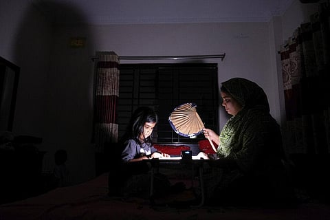 A Bangladeshi woman uses a traditional hand fan as she assists her daughter in her studies during a power cut at their home in Dhaka, Aug. 23, 2022. (File Photo | AP)