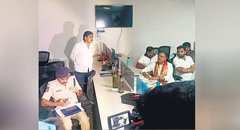 Congress leader Mallu Ravi watches as a police officer checks the documents at Sunil Kumar’s office on Tuesday