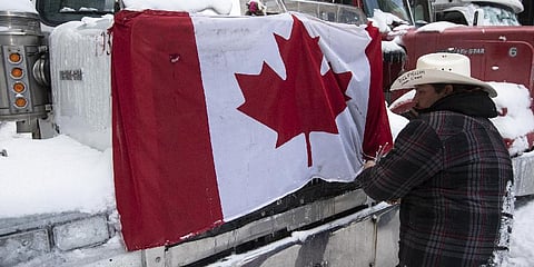 A trucker removes a flag of Canada from the hood of their vehicle as truckers prepare to drive away  after police intervention.(Photo | AP)