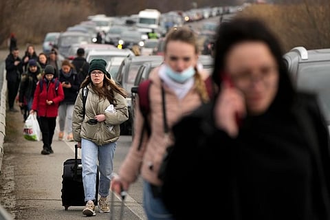 Ukrainian refugees walk along vehicles lining-up to cross the border from Ukraine into Moldova, at Mayaky-Udobne crossing border point near Udobne, Ukraine. (Photo |AP)