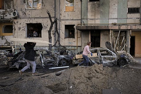 People carry wooden boards to cover the windows of a building damaged by a bombing the previous day in Kyiv, Ukraine. (Photo | AP)
