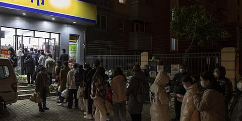 Residents wearing face masks to help protect from the coronavirus line up outside a supermarket at night to buy groceries on Sunday, March 27, 2022, in Shanghai, China.(Photo | AP)