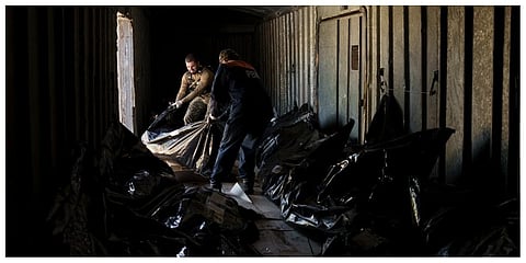 A Ukrainian serviceman and a worker carry the body of a Russian soldier into a refrigerated train in Kharkiv, Ukraine. (Photo | AP)