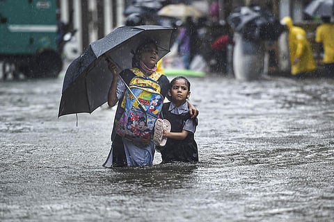A school girl with her guardian wades through a flooded street following heavy monsoon rains in Mumbai. (Photo | PTI)