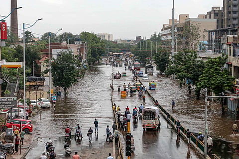Commuters wade through a waterlogged road after heavy rain in Ahmedabad, on July 11, 2022. (Photo | PTI)