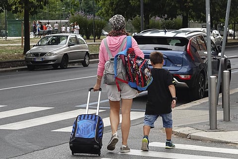 A woman carries backpacks as her son walks after coming out of a primary school, in Milan, Italy, Wednesday, Sept. 14, 2022. (Photo | AP)