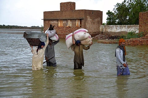 A displaced family carry belongings as they wade through a flooded area after heavy rainfall, in Jaffarabad, a district of Pakistan's southwestern Baluchistan province. (Photo | AP)