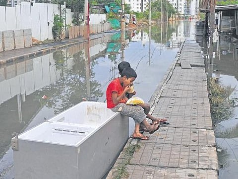 Children eat seated on a defunct refrigerator on a flooded street in Bellandur |  Vinod Kumar T