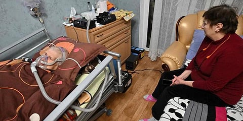A Ukrainian woman sits next to her husband breathing with the help of a ventilator in their flat in Kyiv