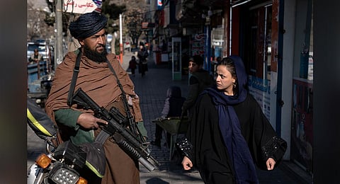 A Taliban fighter stands guard as a woman walks past in Kabul, Afghanistan. (Photo | AP)