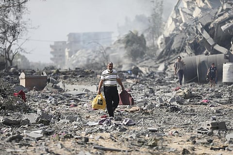 Palestinians walk by the buildings destroyed in the Israeli bombardment on al-Zahra, on the outskirts of Gaza City, Friday, Oct. 20, 2023. (Photo | AP)