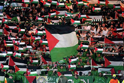 Celtic fans in the stands wave Palestinian flags ahead of the Champions League Group E match between Celtic Glasgow and Atletico Madrid, at Celtic Park in Scotland on October 25, 2023. (Photo | AP)