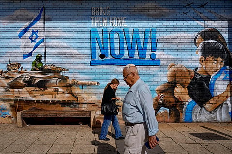 People walk past graffiti calling for the return of the hostages kidnapped during the Oct. 7 Hamas cross-border attack in Israel, in Kfar Saba, Israel, Thursday, Nov. 23, 2023. (Photo | AP)