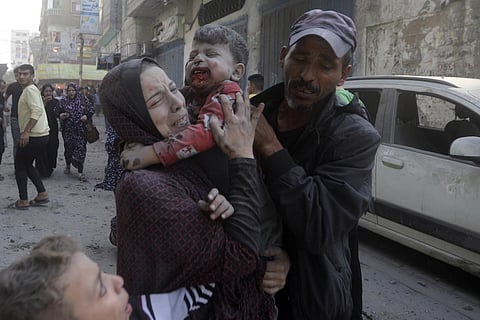 A Palestinian woman cries as she carries her wounded son following an Israeli airstrike in Bureij refugee camp, Gaza Strip. (Photo | AP)
