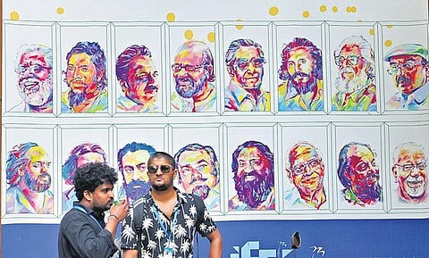 Delegates standing in front of a hoarding that displays photos of legendary Malayalam filmmakers at Tagore Theatre,  the main venue of the International film festival in Thiruvananthapuram, on Sunday