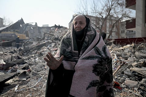 A resident stands covered with a blanket in front of his collapsed building as rescue teams carry out search operations at Elbistan district of Kahramanmaras on February 11, 2023. (Photo | AFP)