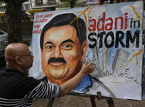 An artist gives final touches to a painting of Indian businessman Gautam Adani, depicting the ongoing crisis of the Adani group, in Mumbai. (Photo | AP)