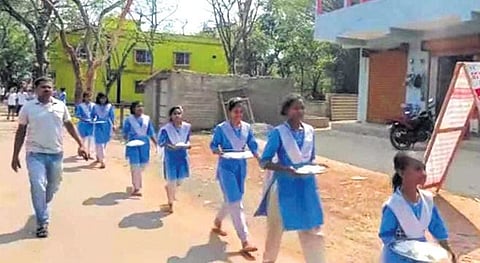 Students walking with plates of rice at Rasgovindpur on Monday | Express