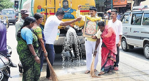 Kamsale Ravi cleans a part of the Jamboo Savari route with water, gomutra and cow dung  in Mysuru on Sunday. (Photo|Udayashankar S)