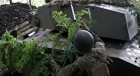 A Ukrainian artilleryman uses tree branches to camouflage a military vehicle at the frontline near the town of Bakhmut, Donetsk region.  (Photo | AFP)