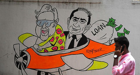 In this photo taken on April 2, 2019, a commuter walks past a wall graffiti displaying cartoons of Indian businessmen turned fugitives Vijay Mallya and Nirav Modi. (Photo | AFP)