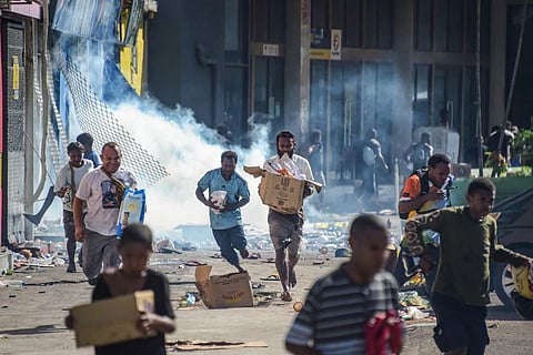 People run with merchandise as crowds leave shops with looted goods amid a state of unrest in Port Moresby on January 10, 2024. (Photo | AFP)