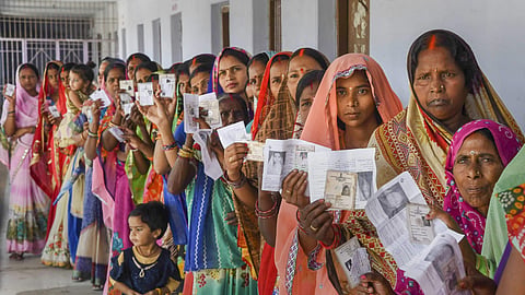 Women show their voter identity cards as they stand in a queue at a polling station.