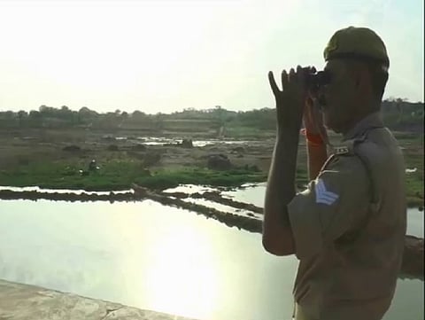 केन नदी पर दूरबीन से पहरेदारी करता पुलिस कर्मी। फोटो: प्रियंका पांडे 