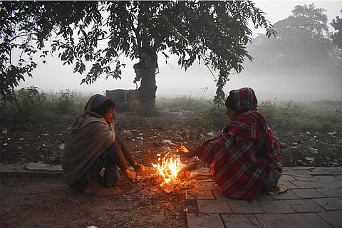भीषण सर्दी में आग के सामने बैठ अपने आप को गर्म रखने का प्रयास करते स्थानीय; फोटो: आईस्टॉक