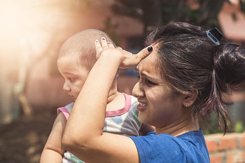 A woman with a baby in her arms shields her face from the sun