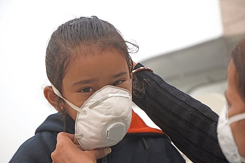 A child’s parent helps her put on a mask. 